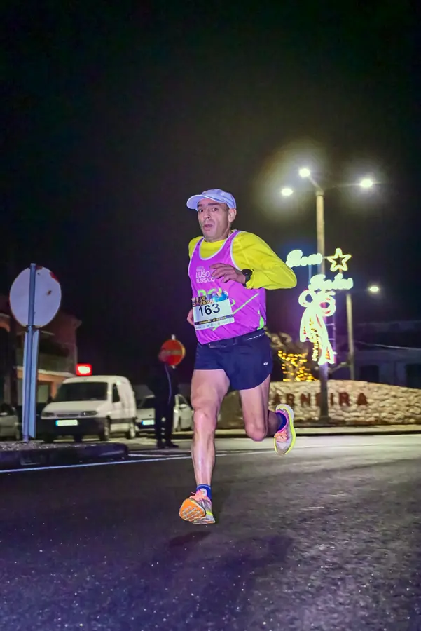 Atleta da São Silvestre a passar junto ao muro com o nome Camarneira, iluminado pelas luzes de Natal.
